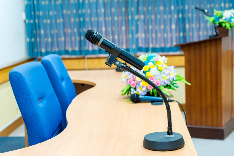 Image of a chairman microphone unit with a priority button and gooseneck mic on a boardroom table.